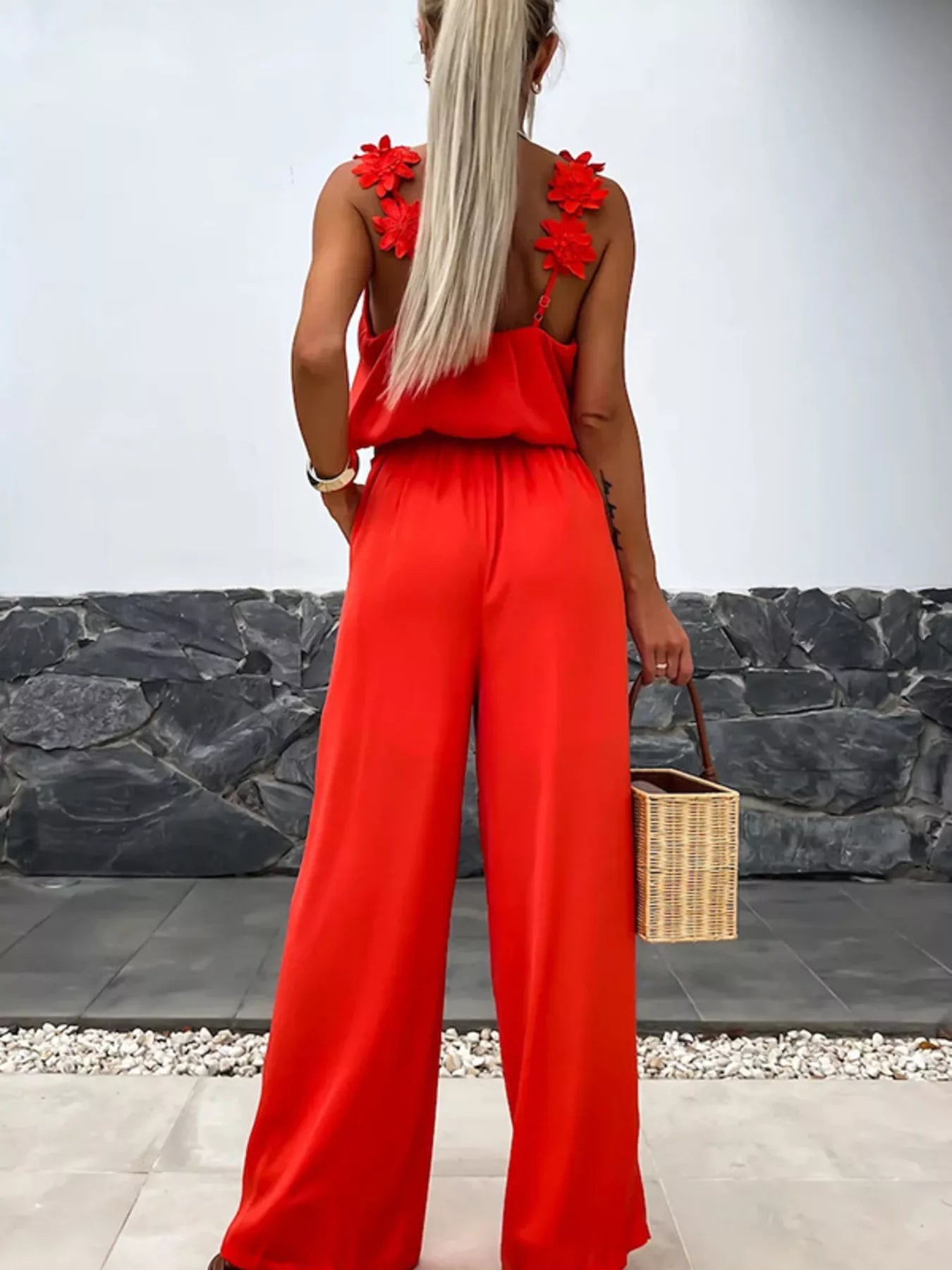 Red floral-appliqué wide-leg jumpsuit; back view shows flower-embellished straps and a wicker basket bag.