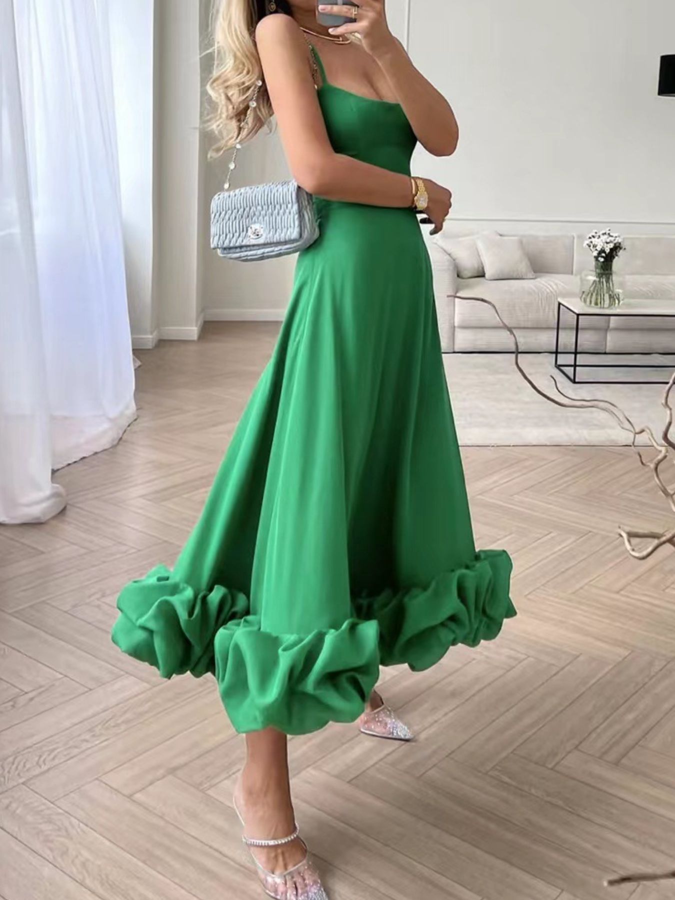 Ruffle-hem green scoop-neck midi dress with thin straps, paired with a light blue quilted handbag.