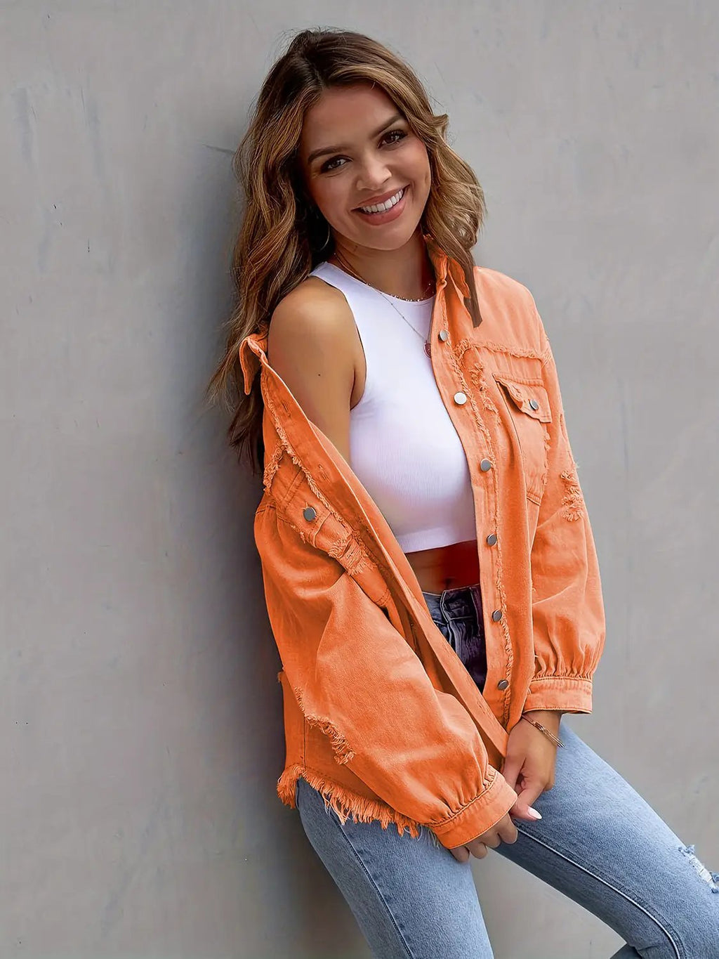Distressed drop-shoulder denim jacket in bright orange worn over a white top, frayed hems, oversized fit