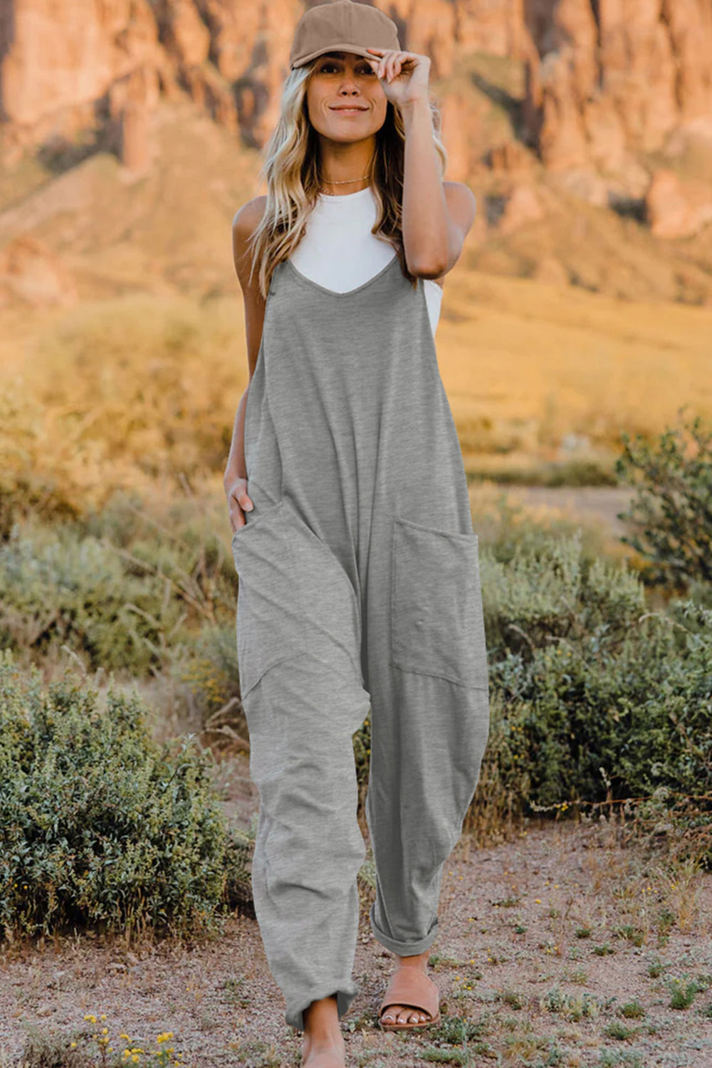Double Take V-Neck Sleeveless Jumpsuit with Pockets in grey by Belle Bijouix, worn by a model in a desert landscape.