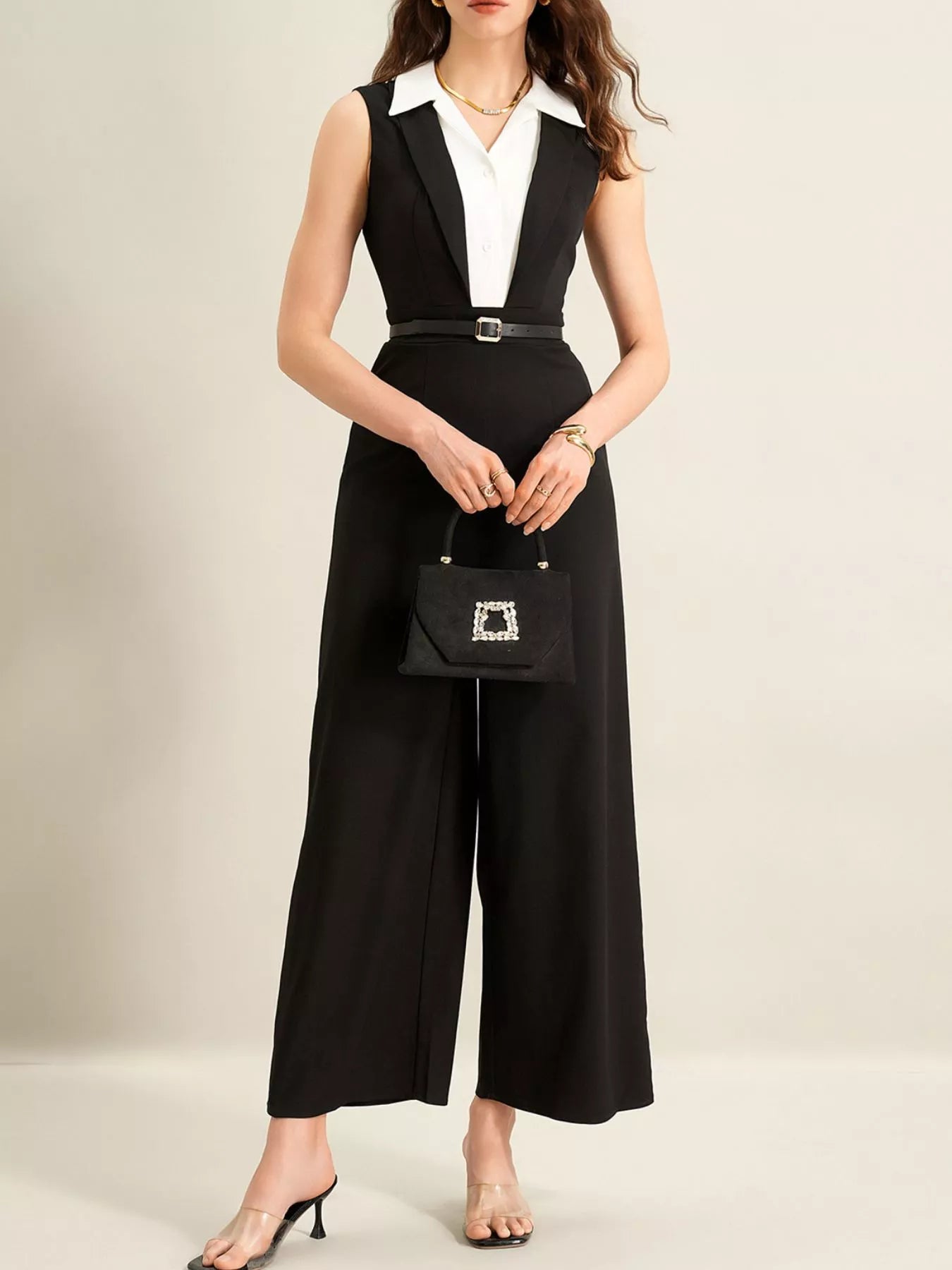 Sleeveless black wide-leg jumpsuit with white collar detail, belted, paired with a small black handbag