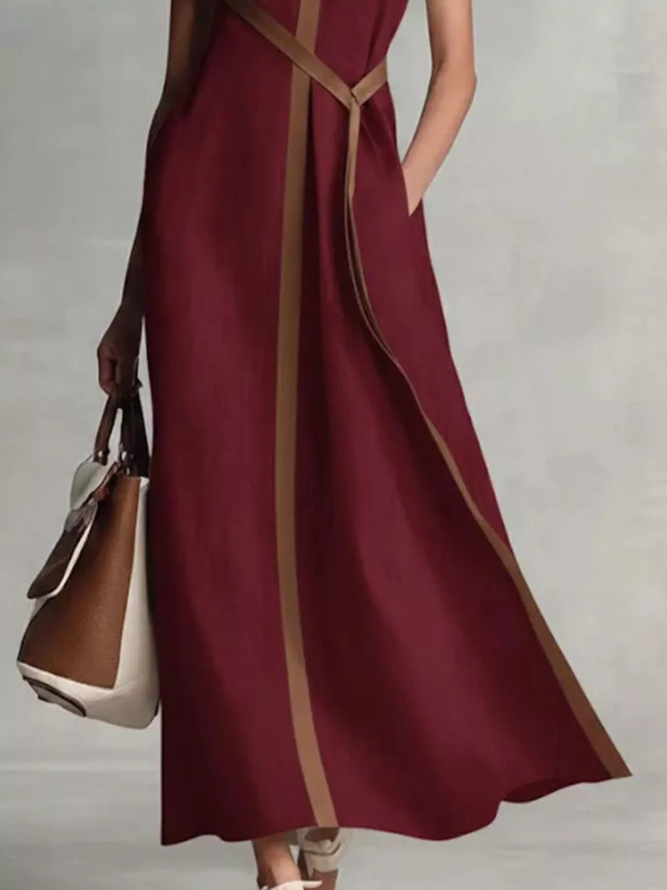 Sleeveless burgundy maxi dress by Trendsi, plus-size, with tan contrast trim along edges and hem, shown with a white handbag