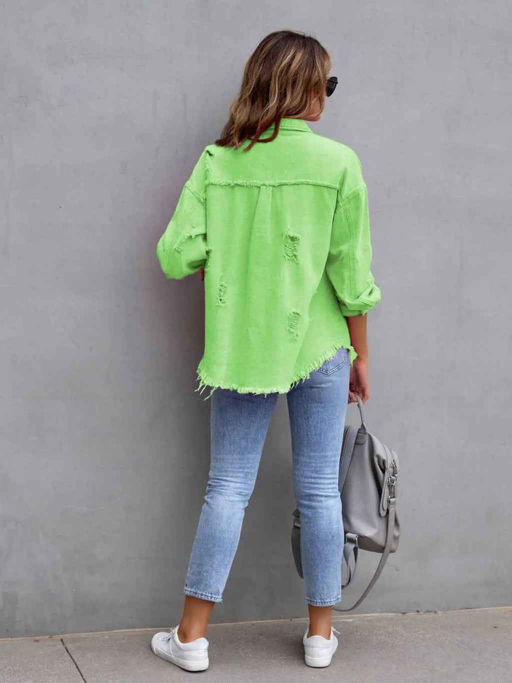 Denim jacket neon green distressed drop-shoulder with frayed hem worn by woman in light-wash jeans