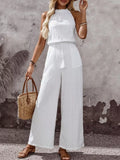 Plus-size white tassel-waist halter-neck sleeveless wide-leg jumpsuit with drawstring, paired with a straw handbag.