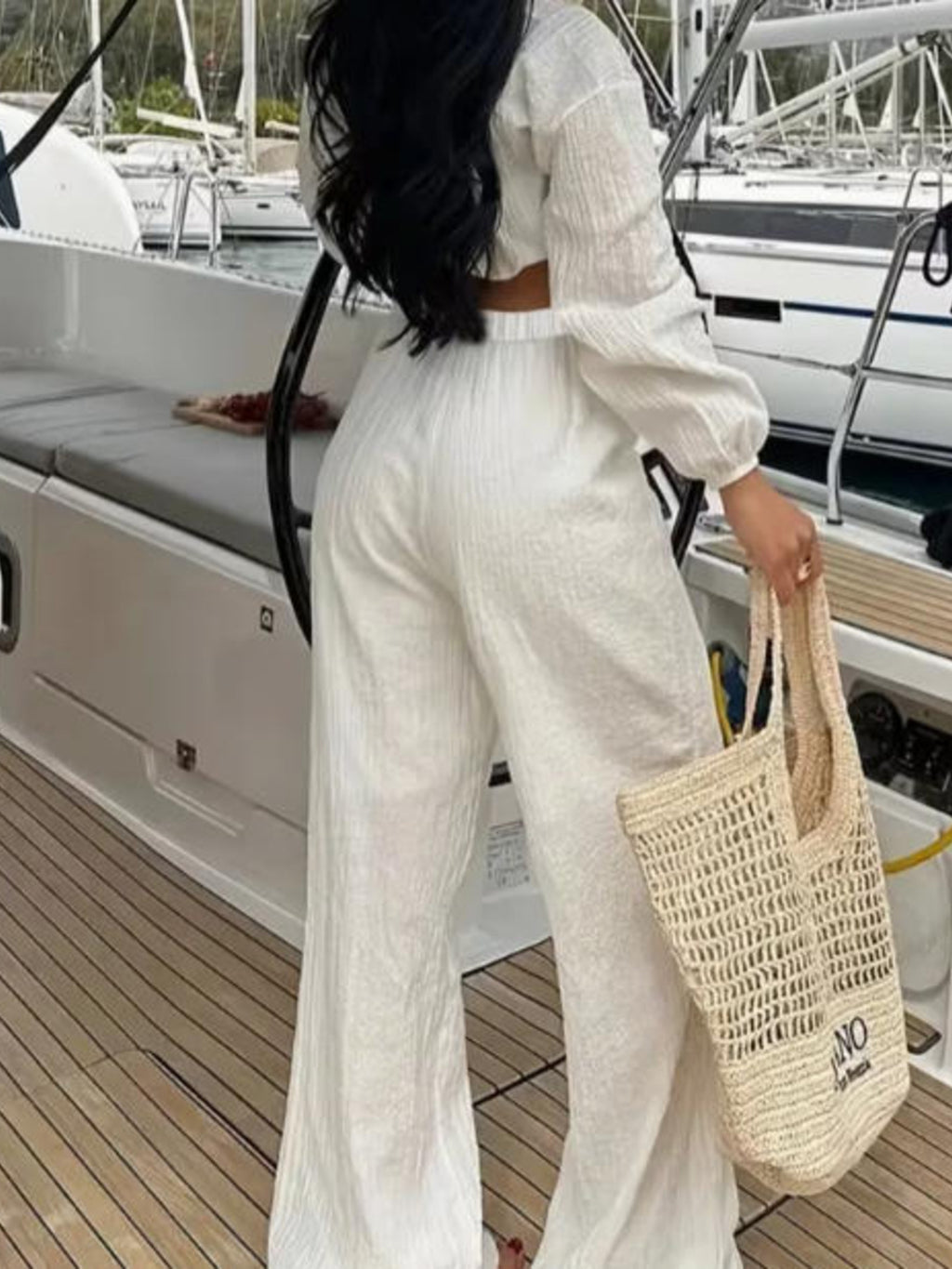 Textured tie-front crop top and wide-leg pants set in cream; model on a yacht deck with a woven tote.
