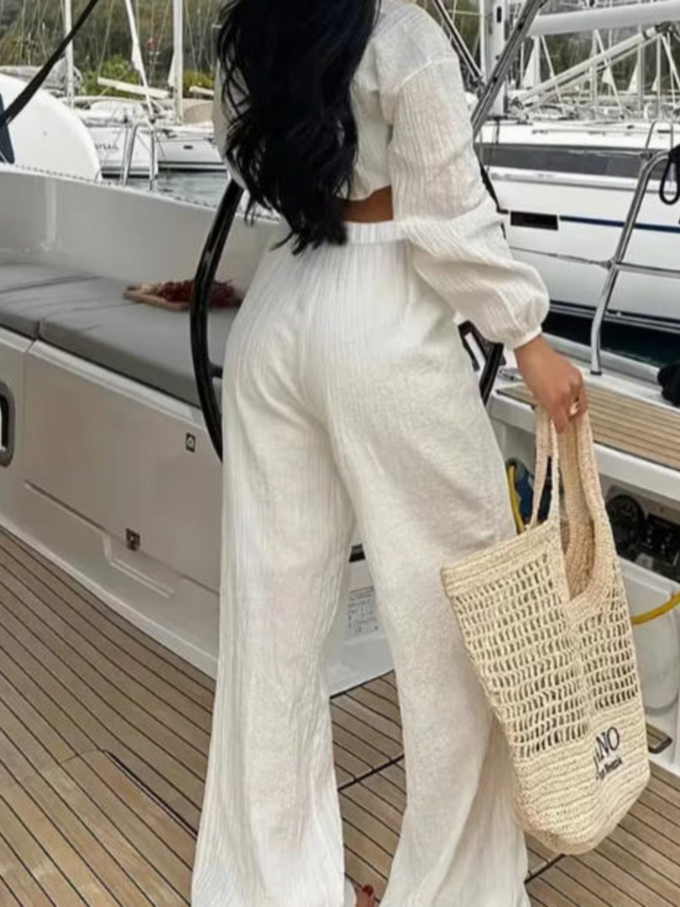 Textured tie-front crop top and wide-leg pants set in cream; model on a yacht deck with a woven tote.