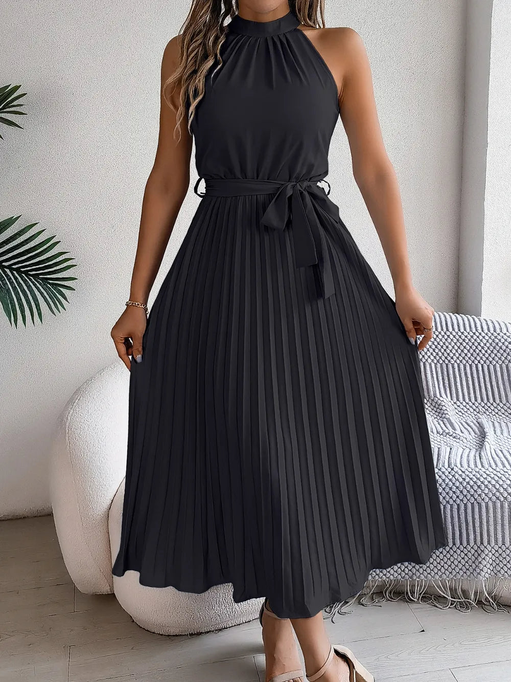 Pleated tie waist sleeveless midi dress in black with halter-neck, bow waist tie, flowing pleated skirt.