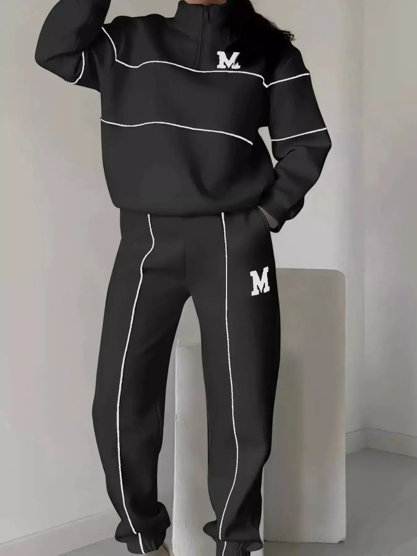 Plus-size two-piece Belle Bijouix black activewear set with white piping, zip top and pocketed pants; M logos on chest.