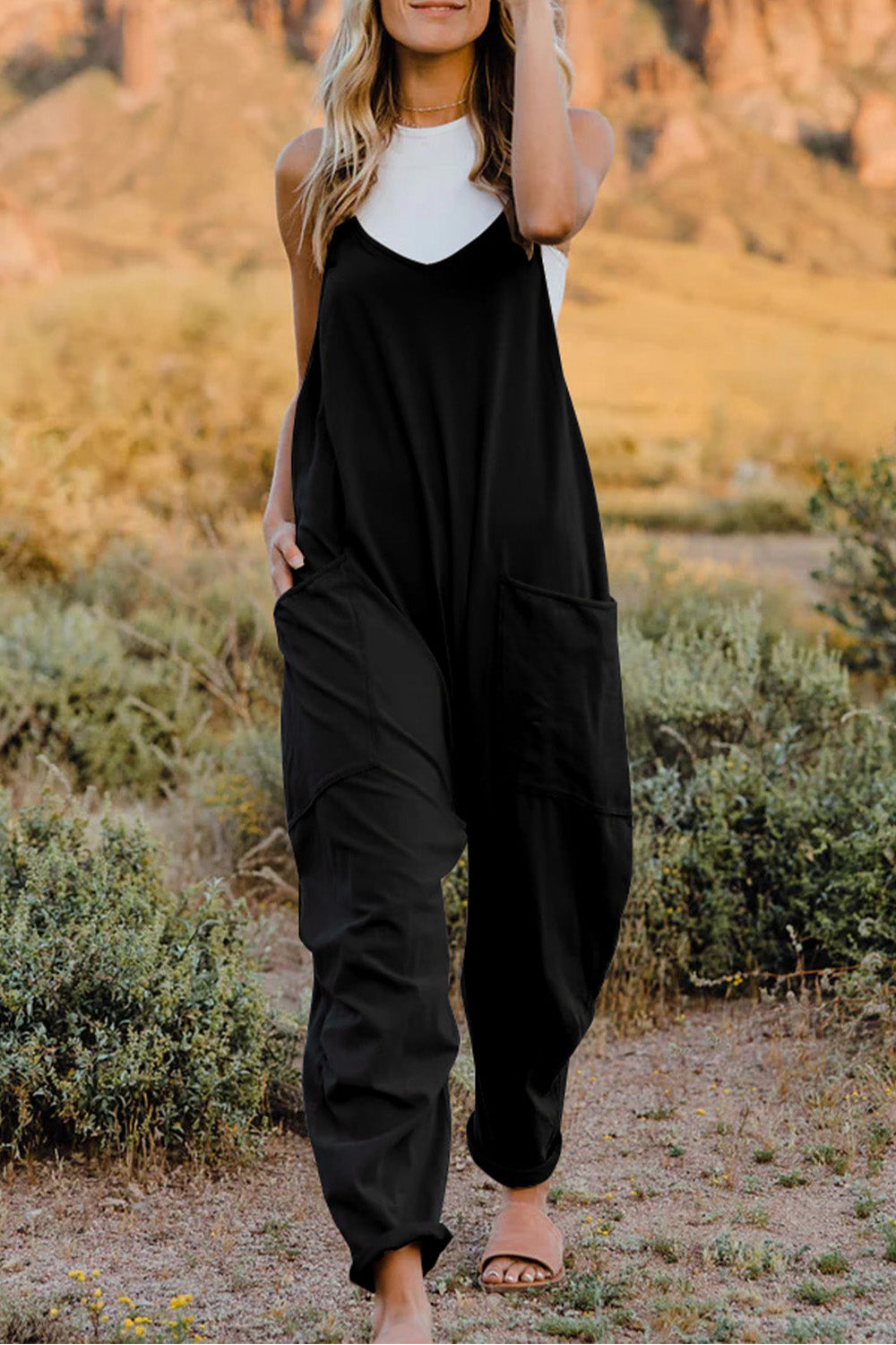 Double Take full-size V-neck sleeveless jumpsuit with pockets, black, worn over a white top outdoors.