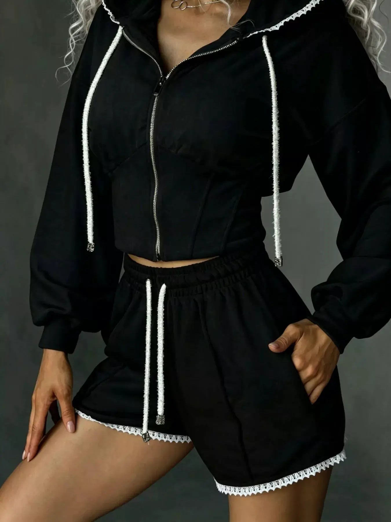 Two-piece activewear set: black zip-up hooded jacket with white drawstrings and lace trim, matching shorts.
