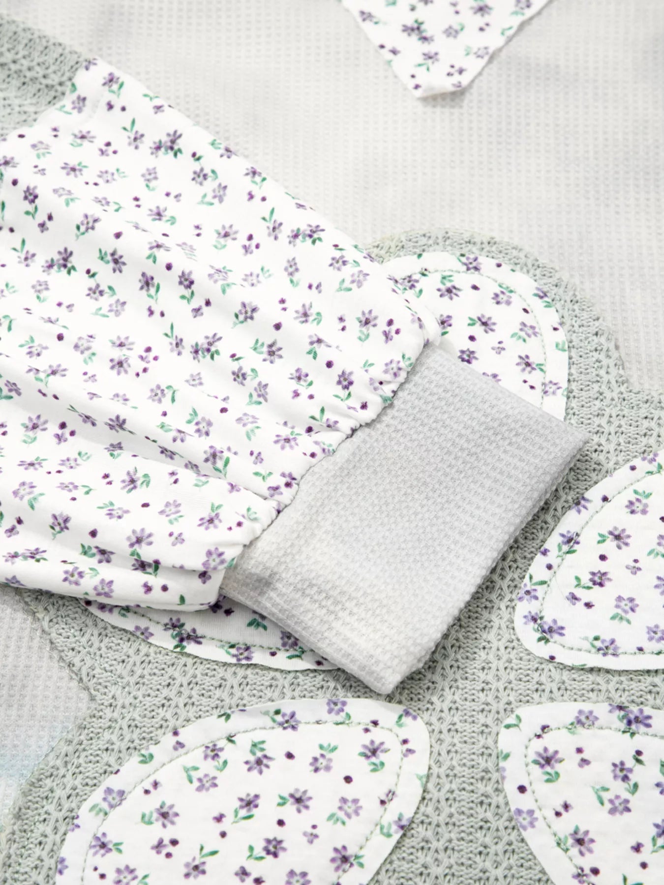 Floral patched waffle-textured hoodie sweater with white base, purple flowers, and gray knit cuffs