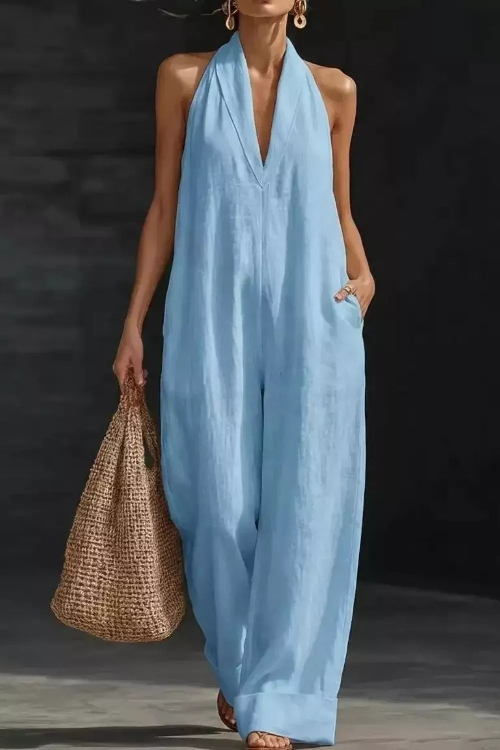 Sleeveless light-blue wide-leg jumpsuit with halter neckline and pockets, paired with a woven tote bag.