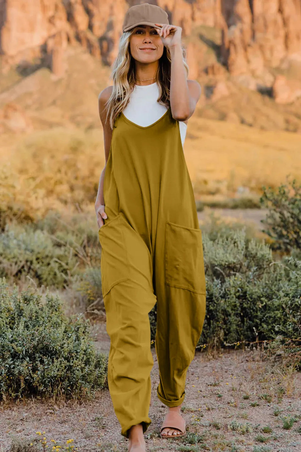 Double Take full-size V-neck sleeveless jumpsuit with pockets in olive green, worn by model in a desert landscape