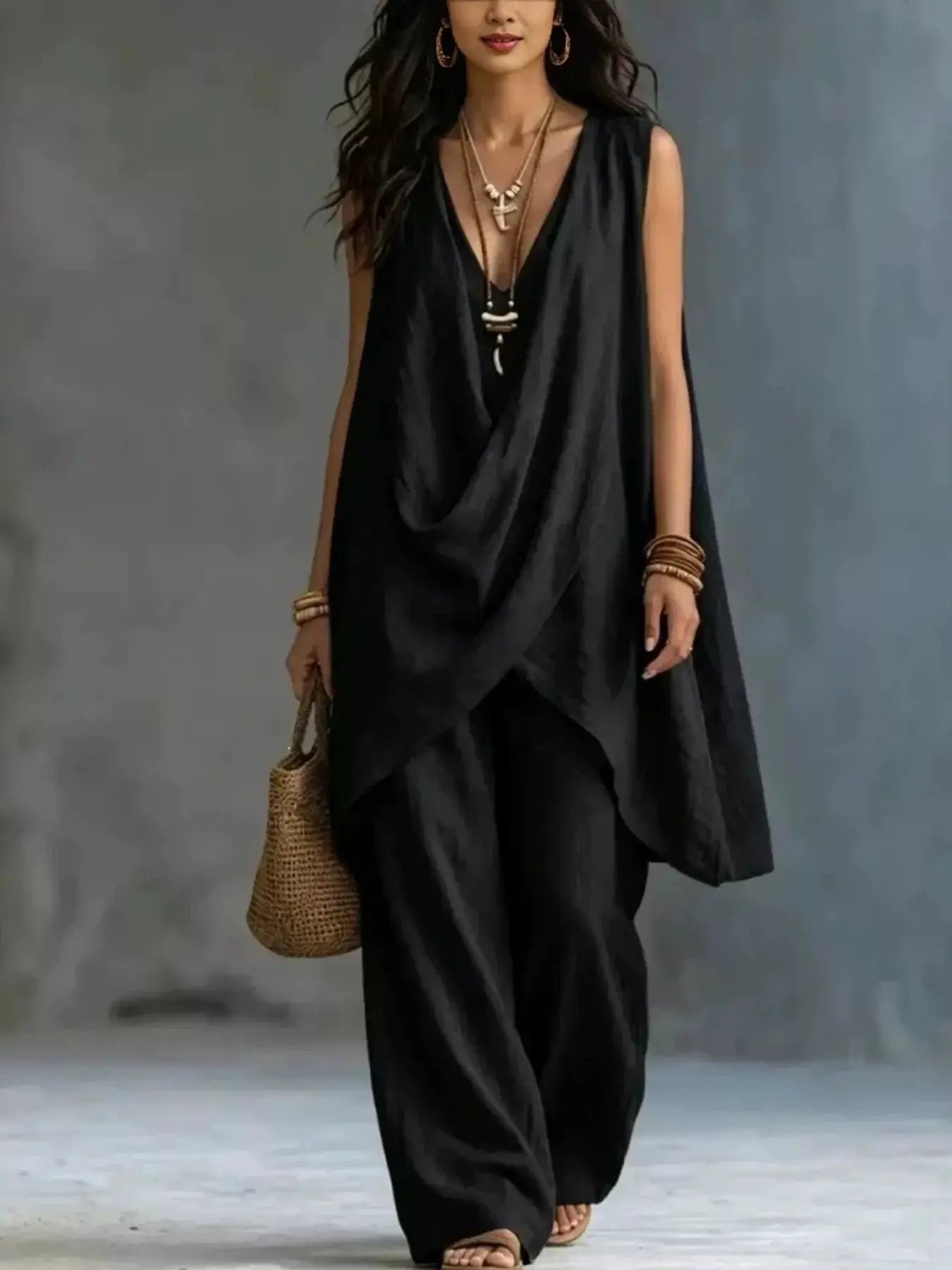 Sleeveless Asymmetrical Top and Wide-Leg Pants Set by Belle Bijouix in black, shown with layered necklaces and a straw bag.