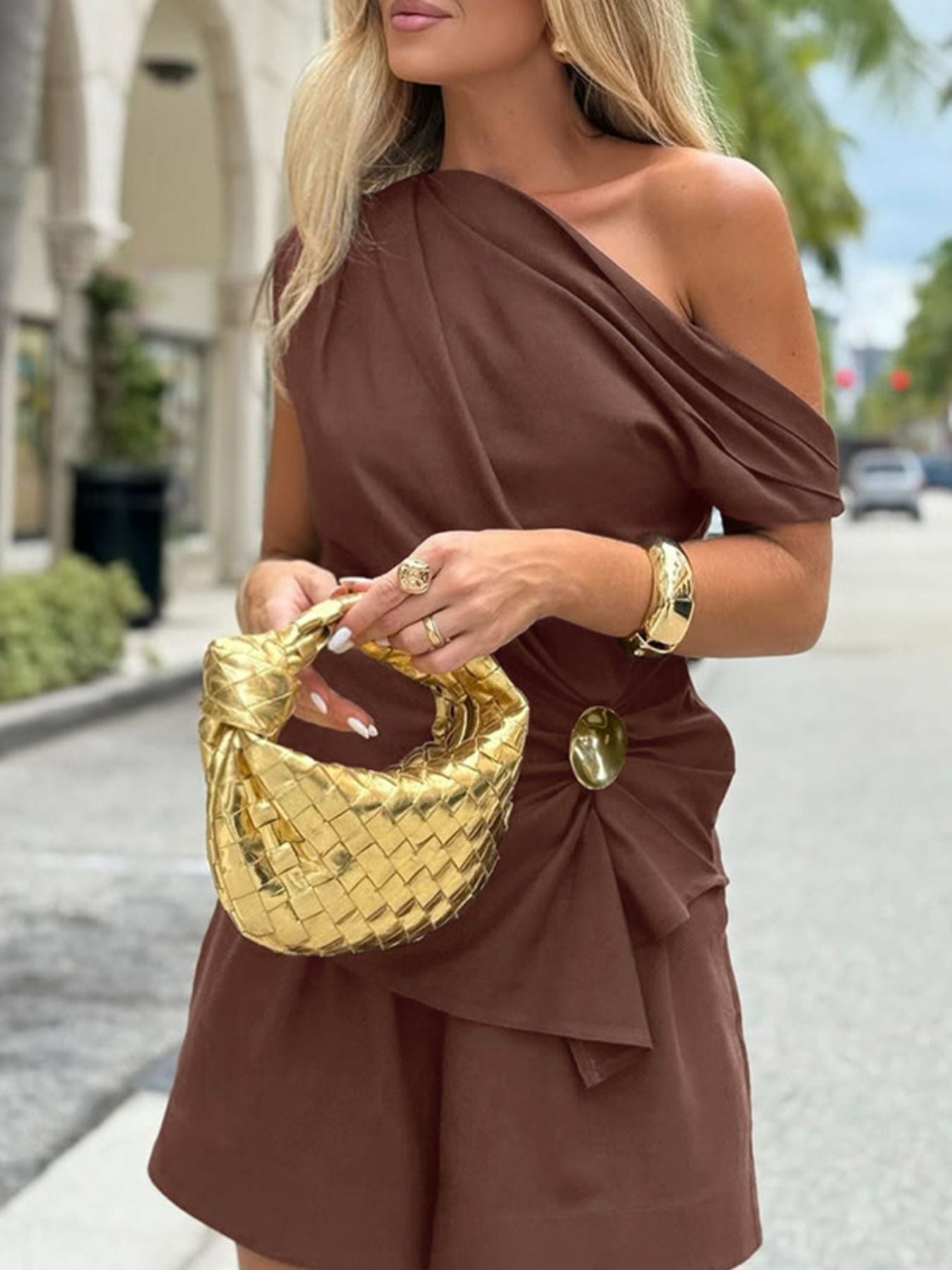 One-Shoulder Top and Shorts Set in brown ruched, asymmetrical design by Belle Bijouix with a gold woven handbag.