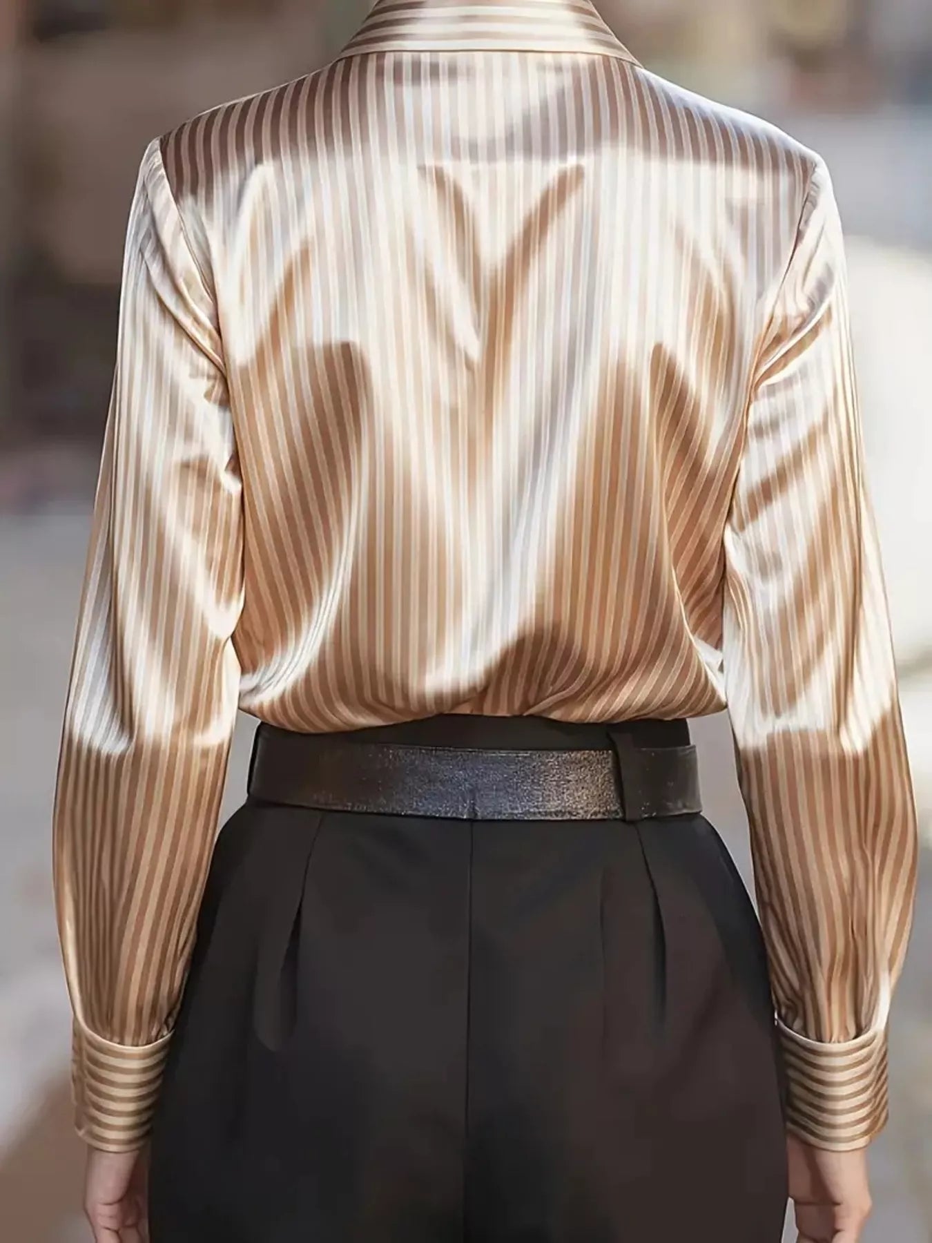 Striped long-sleeve shirt by Belle Bijouix, silky beige-gold stripes, tucked into black trousers with a metallic belt.