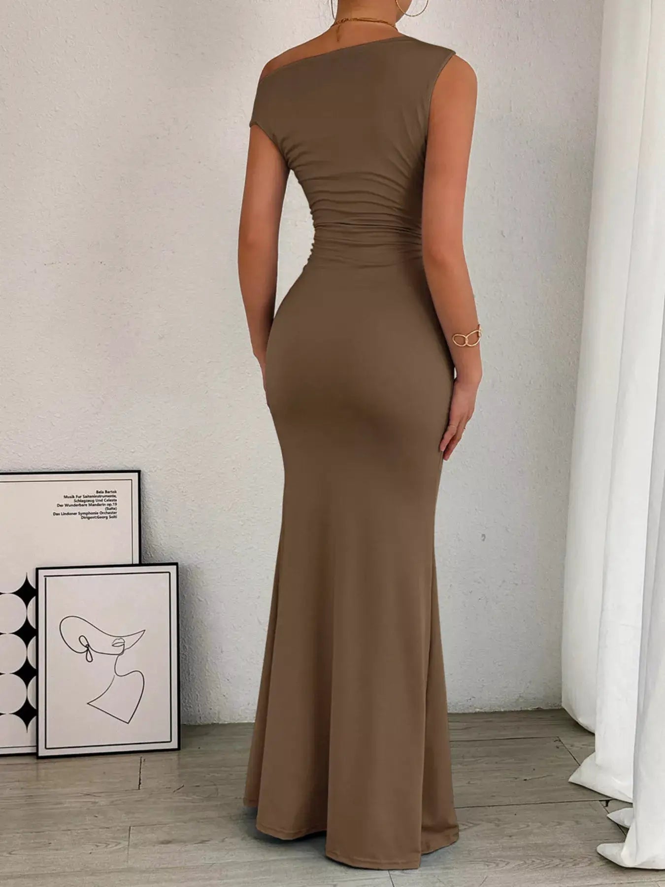 One-shoulder ruched bodycon maxi dress in taupe, back view with a fitted waist and flared hem.