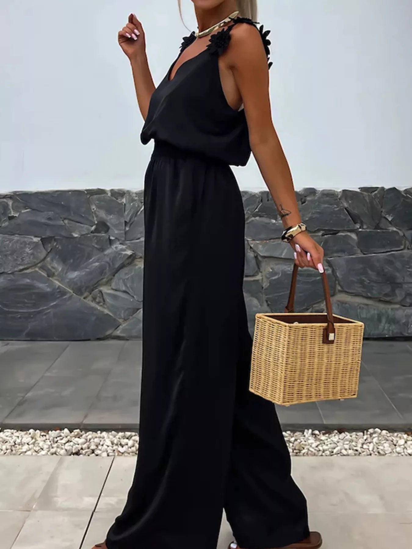 Floral-applique v-neck black wide-leg jumpsuit with shoulder flower accents, paired with a wicker basket bag