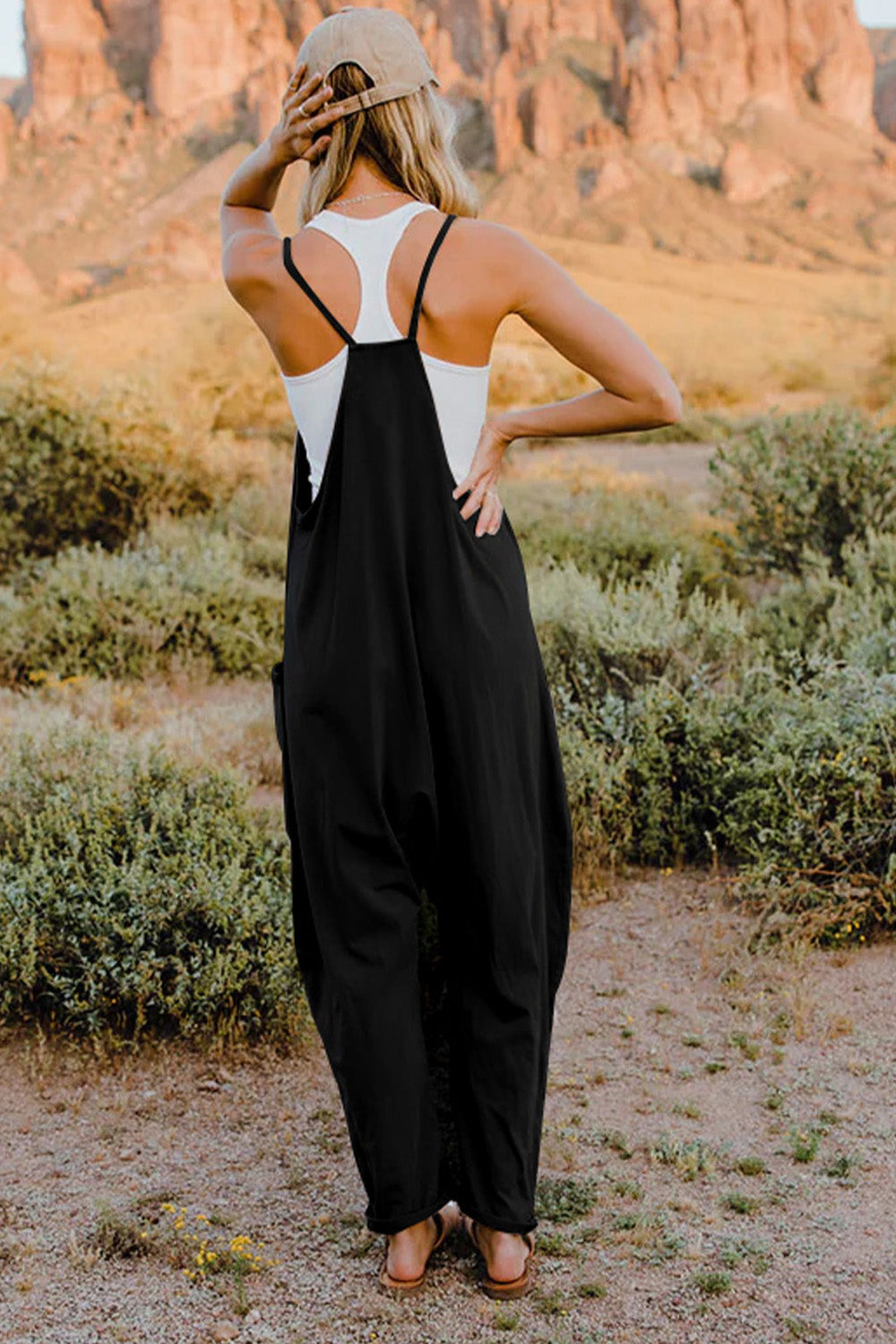 Double Take Full Size V-Neck Sleeveless Jumpsuit with Pockets in black, back view on model in a desert setting