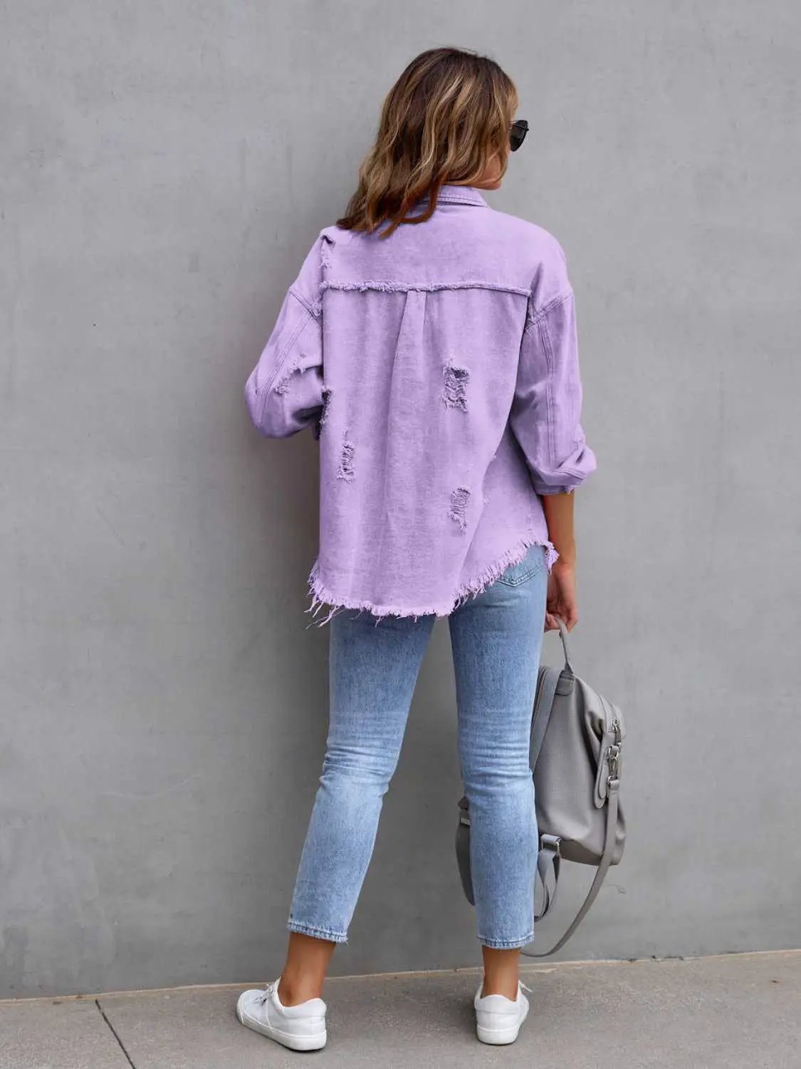 Distressed drop-shoulder denim jacket in lavender with frayed hem and ripped patches, back view on model.
