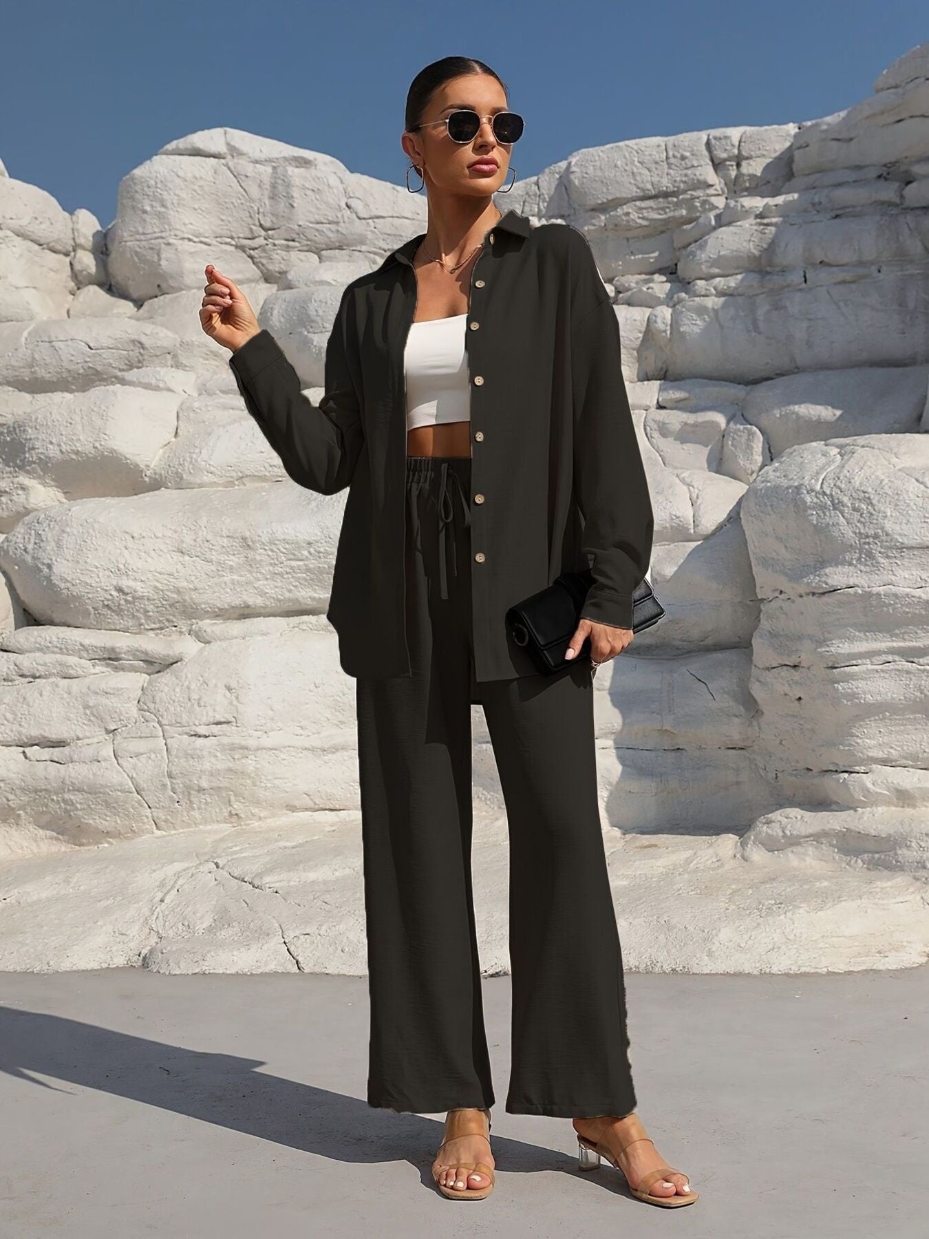 Button Up Long Sleeve Shirt and Pants Set in black; model wears a white crop top, sunglasses, and tan sandals.