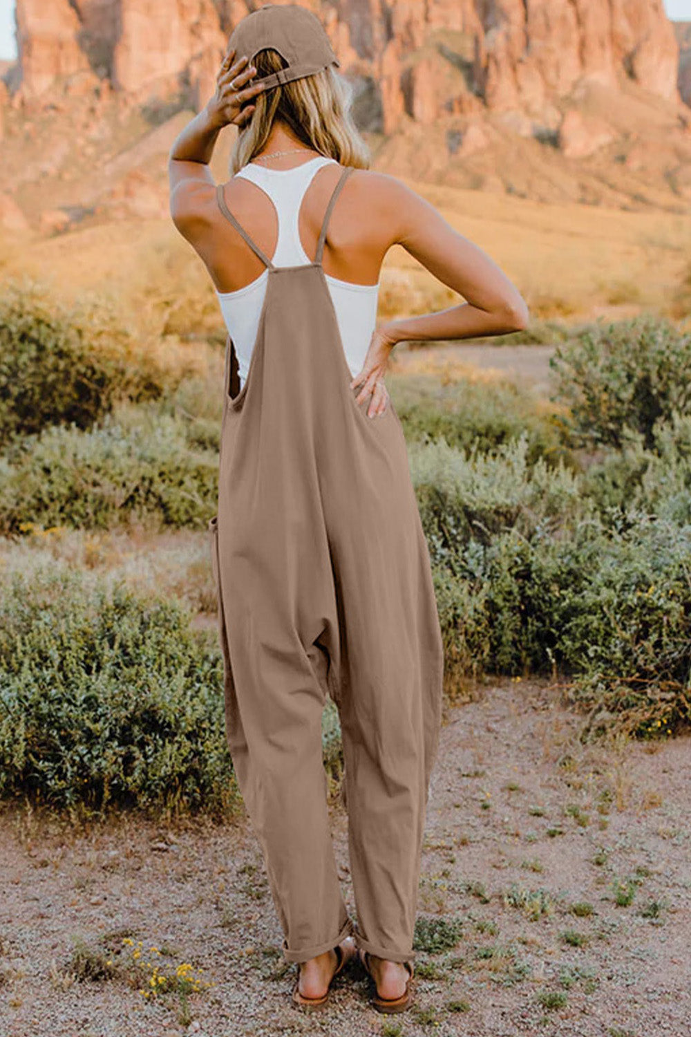 Double Take full-size V-neck sleeveless jumpsuit with pockets in taupe, worn outdoors in a desert setting.