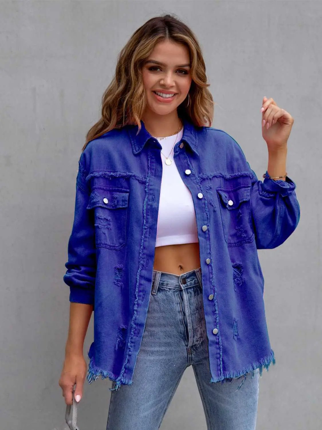 Distressed drop-shoulder denim jacket in blue with frayed hems worn over a white crop top