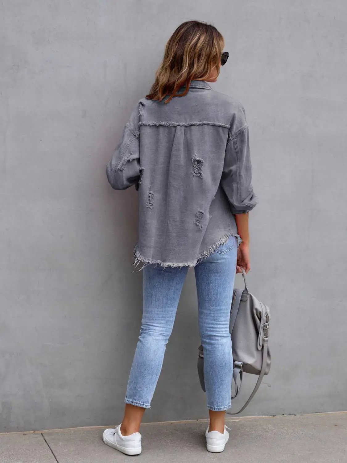 Distressed drop-shoulder denim jacket in gray wash by Belle Bijouix, back view with frayed hem.