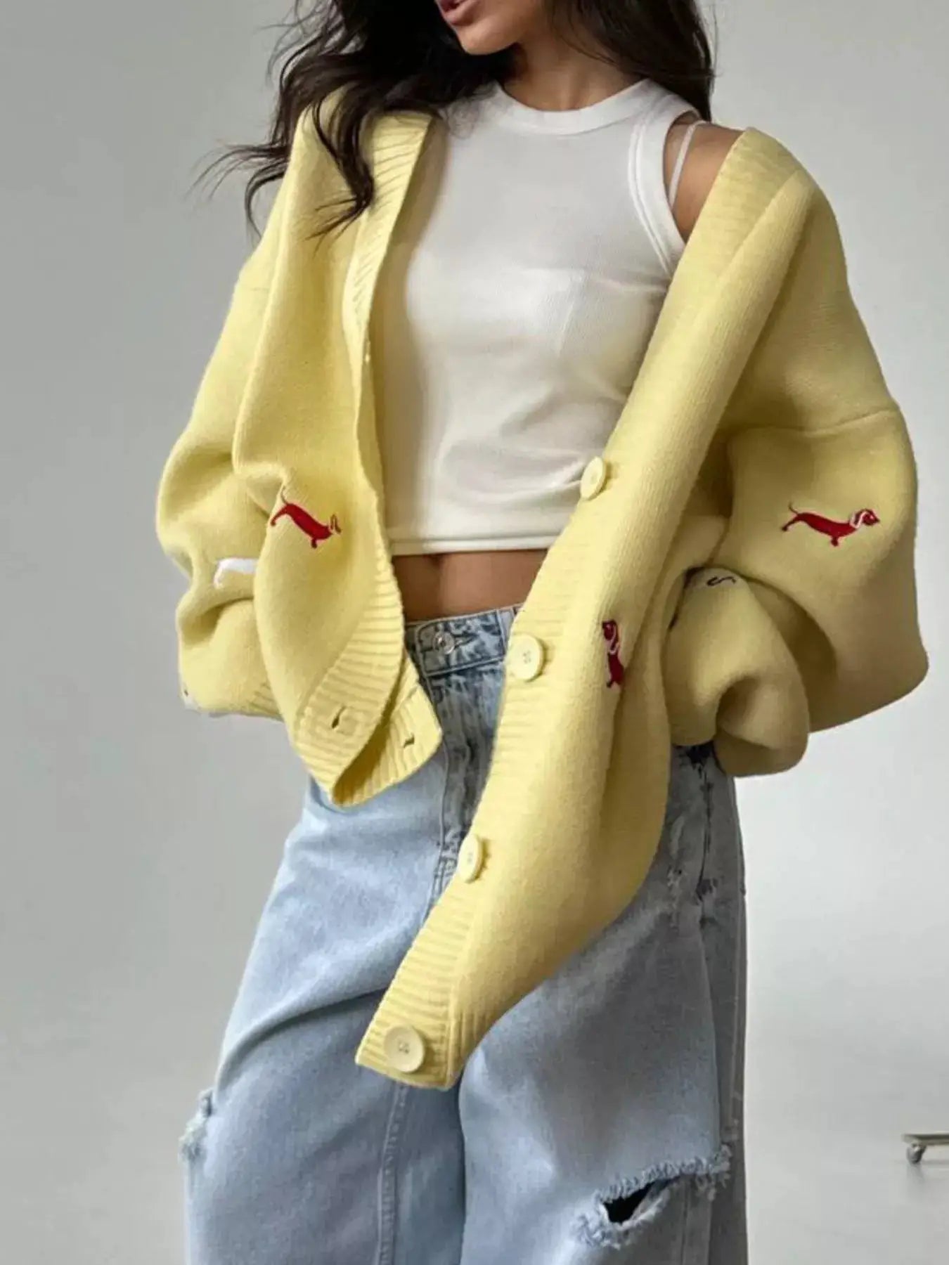 Embroidered button-up cardigan; oversized pale-yellow knit with red embroidery and large cream buttons.