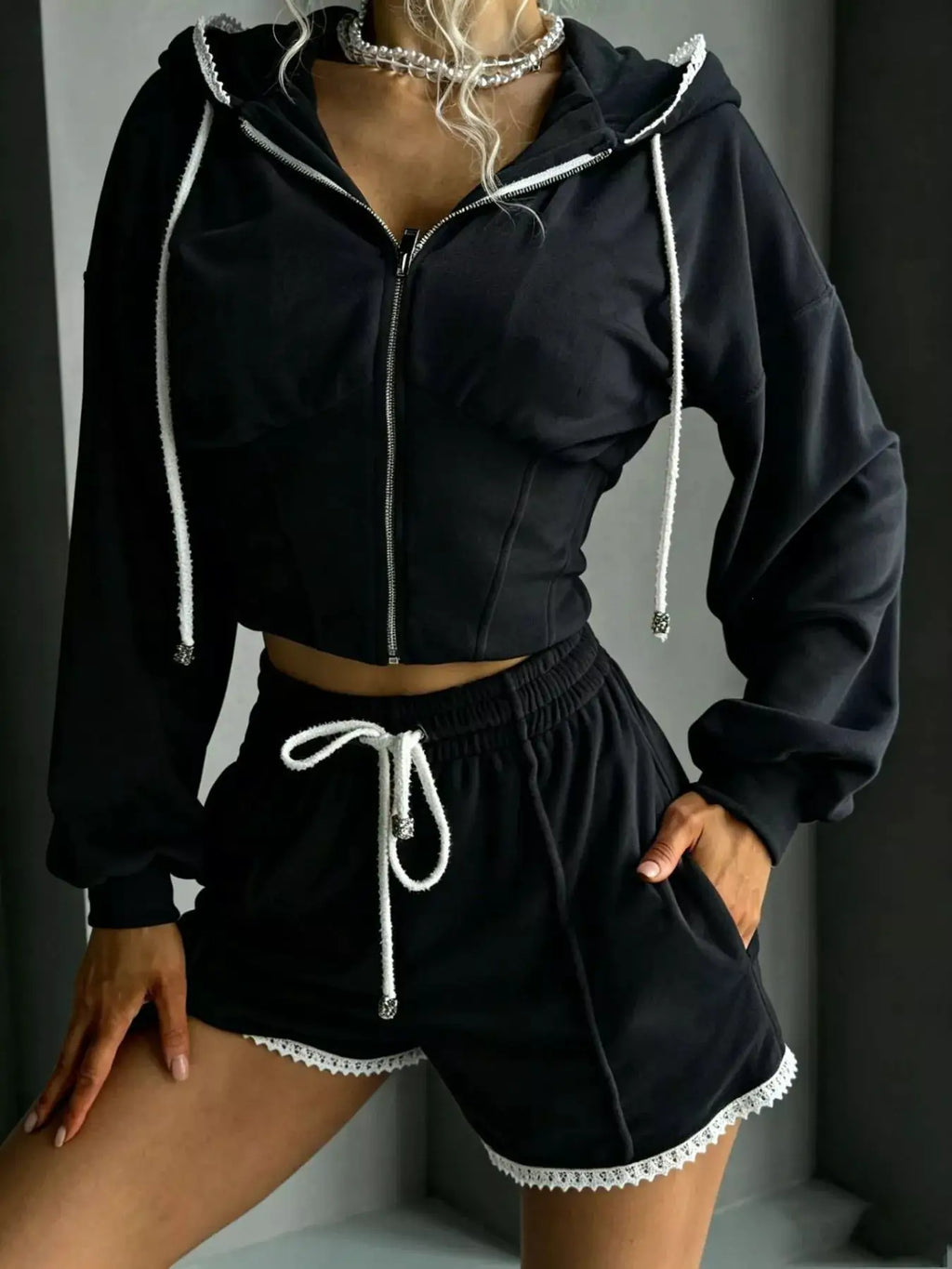 Two-piece black zip-up hooded activewear set with white drawstrings and lace-trim shorts