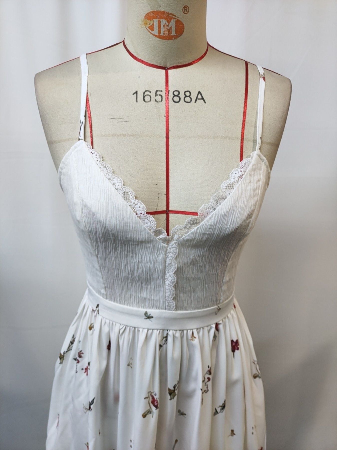 Floral-print lace-trim cami dress on dress form; white bodice with delicate lace along neckline and floral skirt.